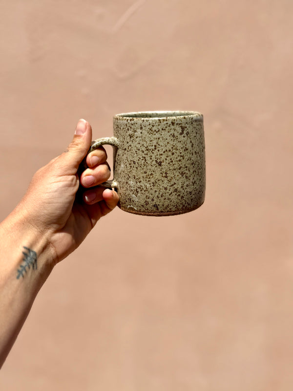 Hand holding a speckled ceramic mug against a beige background